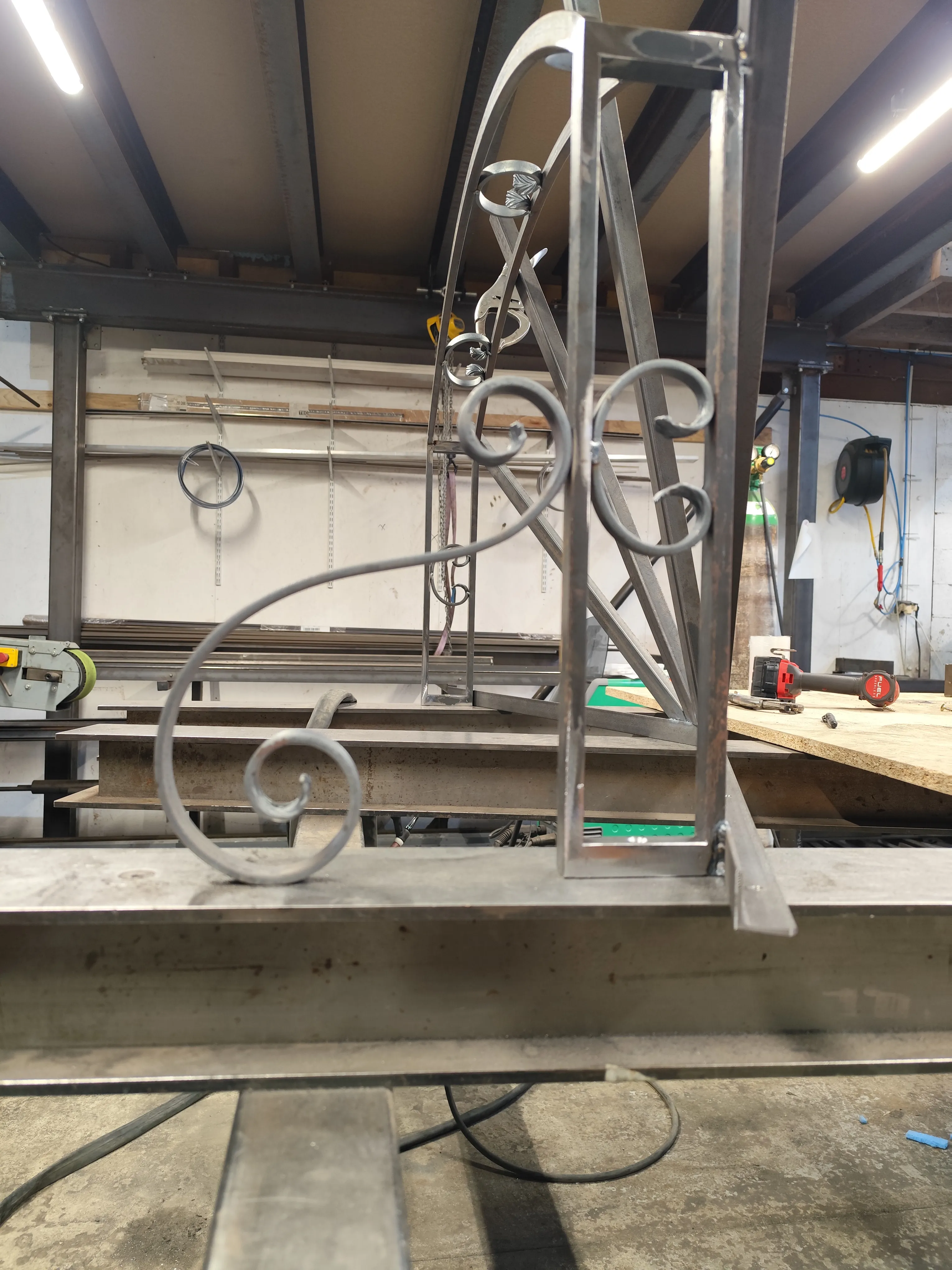 Détail en gros plan d'une volute en acier soudée sur la structure d'une marquise en cours de fabrication dans un atelier de métallerie.