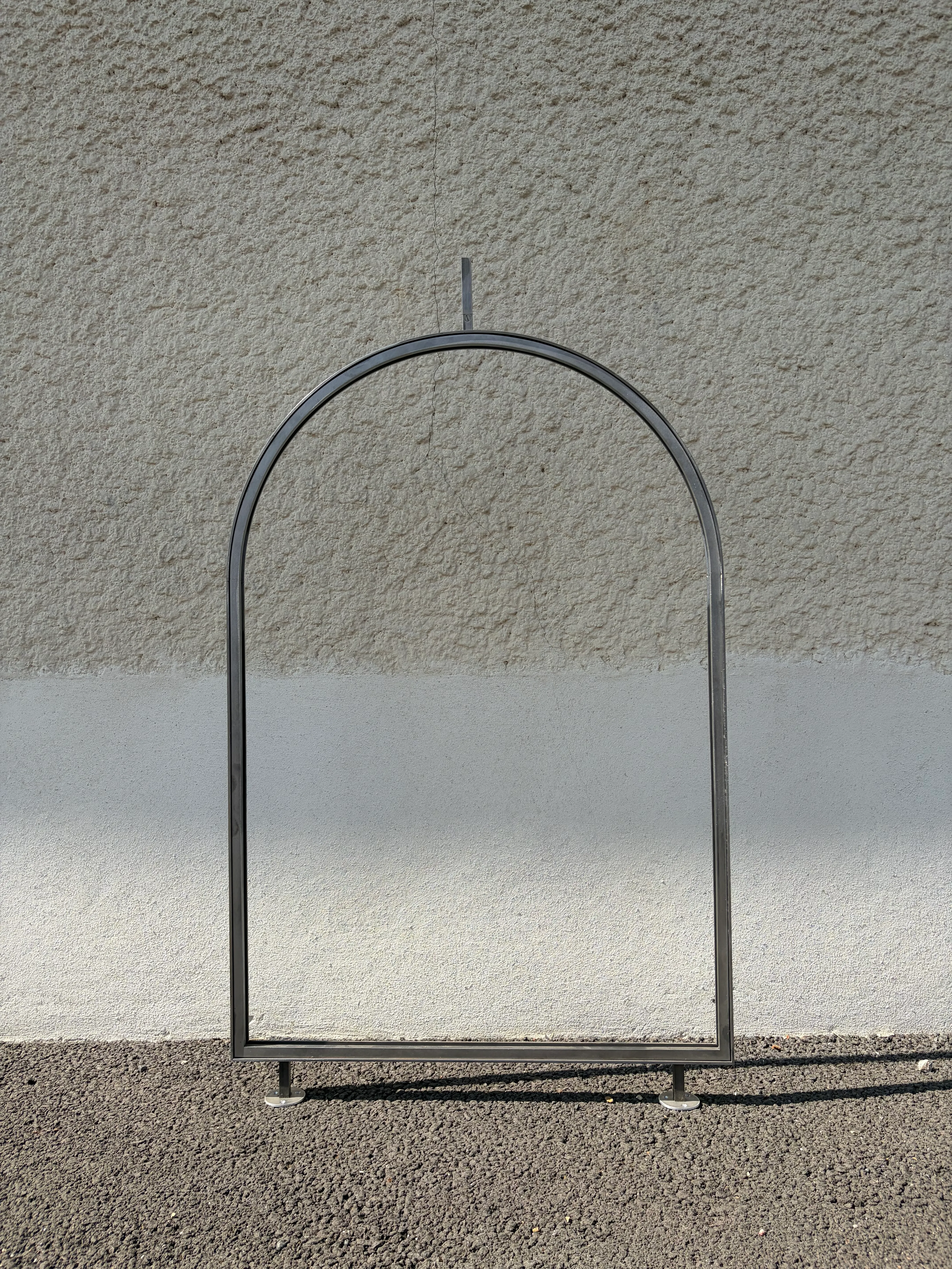 Châssis en acier brut cintré vide, fabriqué sur mesure pour recevoir un vitrail en niche intérieure, posé contre un mur.