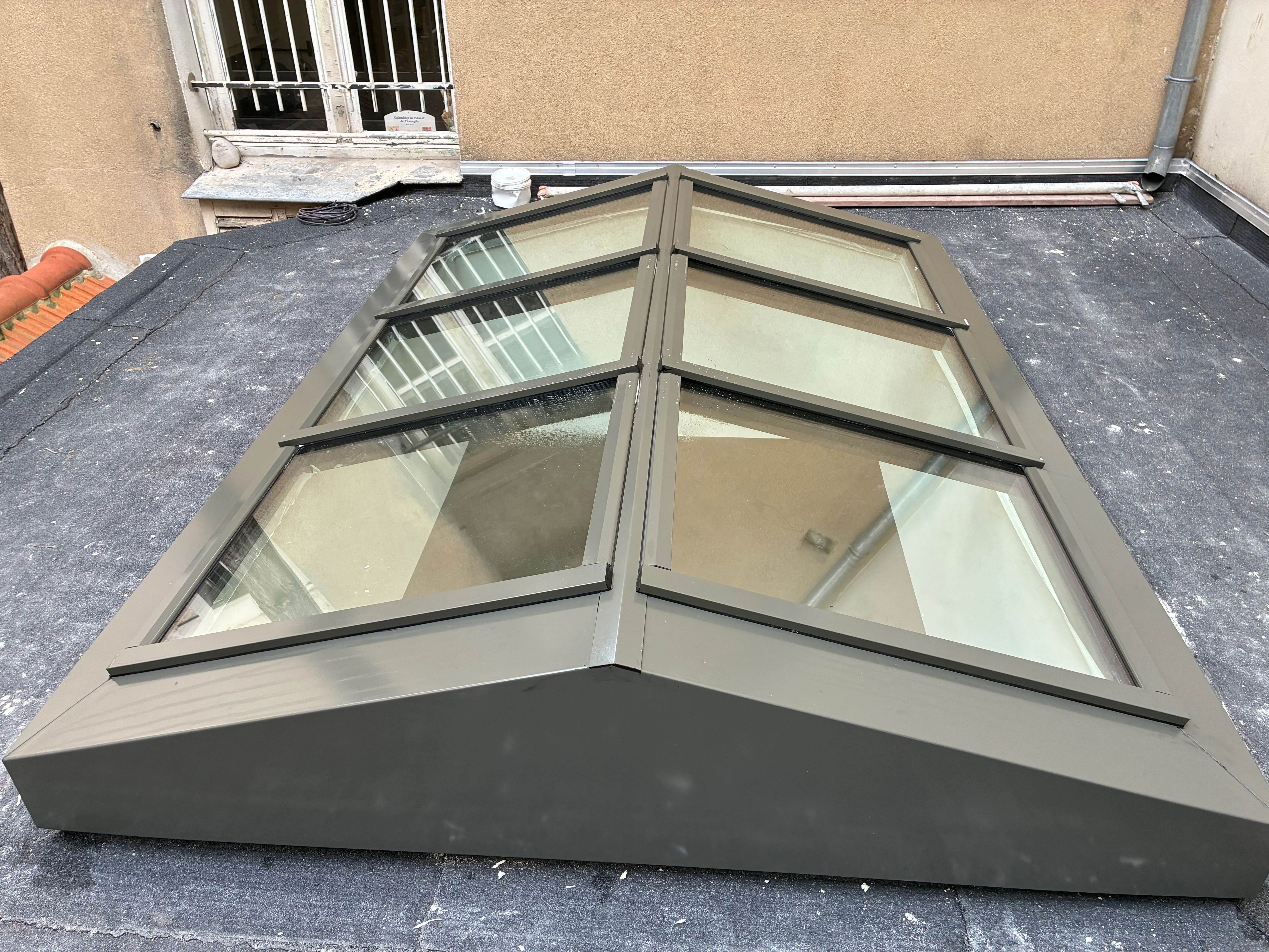 Vue de profil d'une verrière de toit en acier thermolaqué gris anthracite, montrant sa structure angulaire à rupture de pont thermique posée sur une toiture plate.