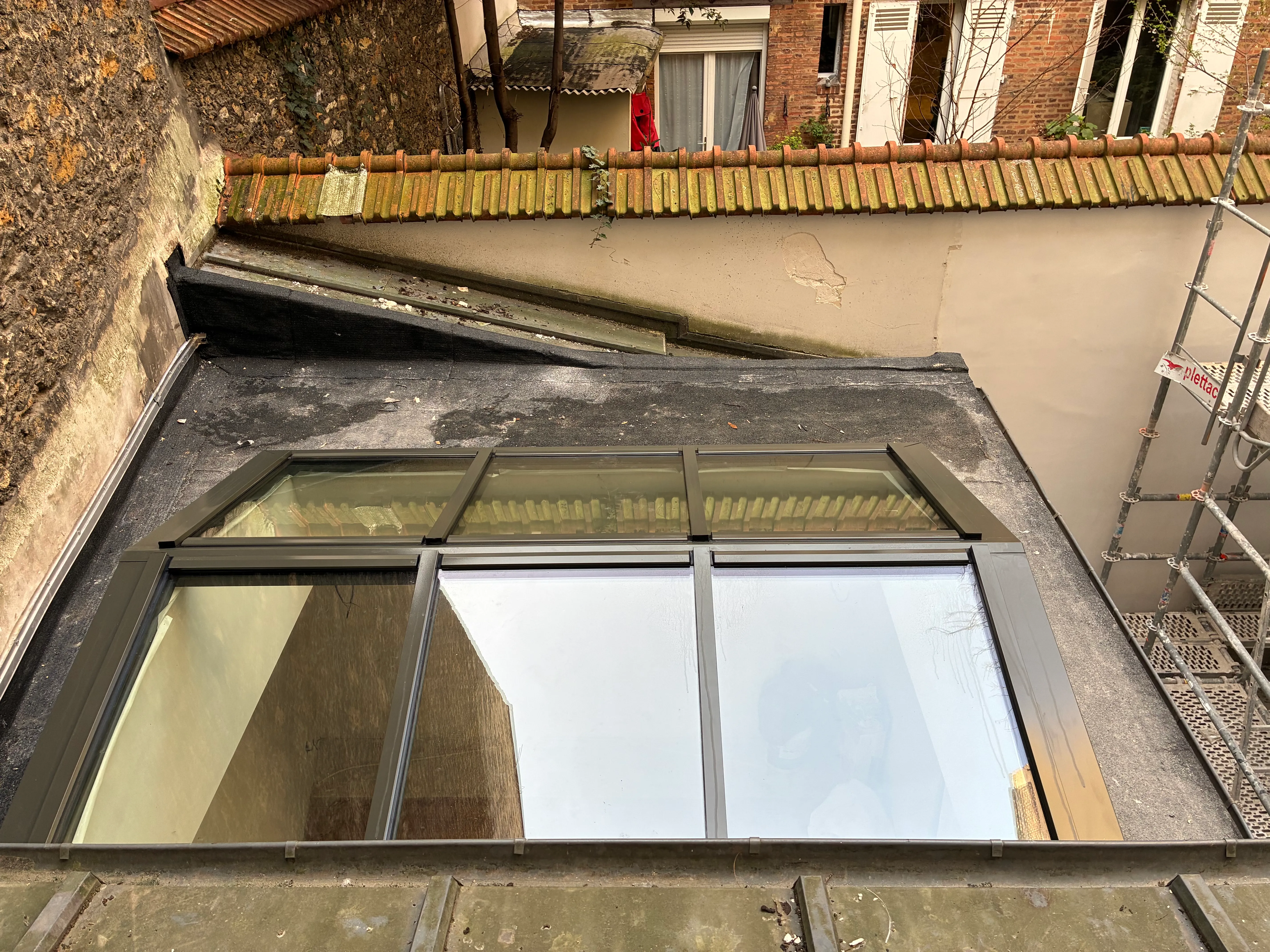 Verrière de toit sur mesure vue de haut, avec un échafaudage métallique visible sur la droite et une façade parisienne traditionnelle en arrière-plan.