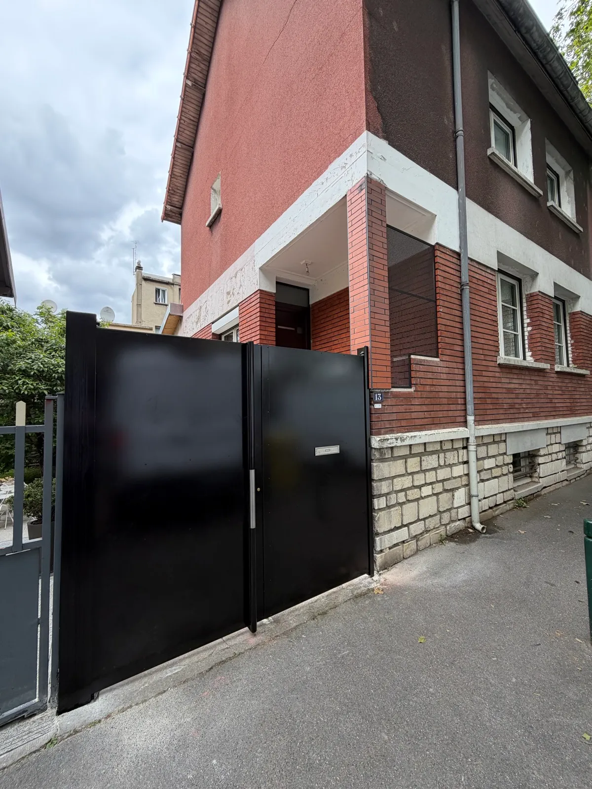 Portail plein en métal noir, installé à l'entrée d'une maison en briques, illustrant une réalisation sur mesure