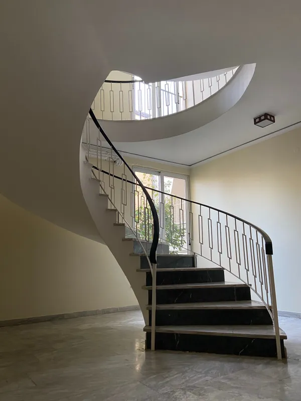 Escalier tournant avec marches en pierre noire et une élégante rampe en ferronnerie blanche aux motifs géométriques