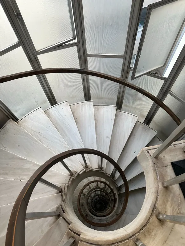 Vue plongeante vertigineuse sur un escalier en colimaçon en marbre blanc, bordé par une main courante continue