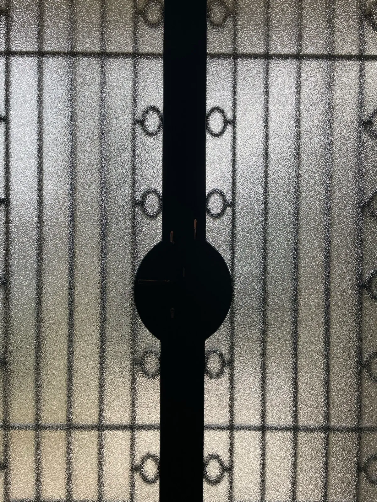 Détail en gros plan d'une porte métallique vitrée, montrant le verre texturé rétroéclairé et la silhouette noire du mécanisme de serrure